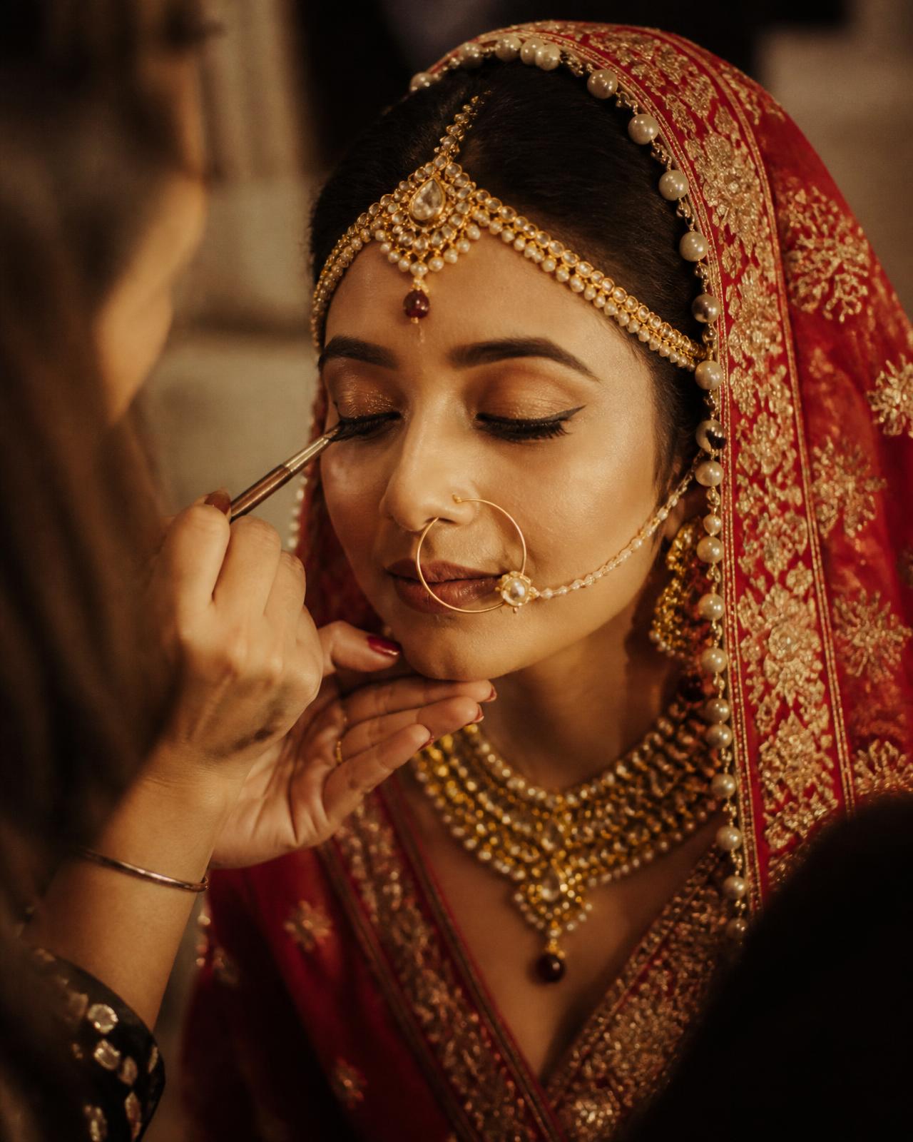 Bridal makeup application at Reshmi Beauty Parlour with gold jewellery and red dupatta